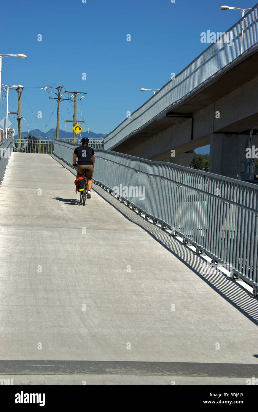 Cyclist riding up ramp onto shared bridge beside new Canada Line light rapid transit commuter rail Stock Photo