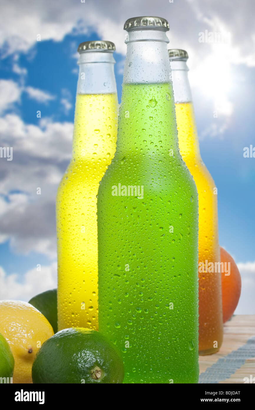 Three ice cold beverages in a wet glass bottles on wooden table with