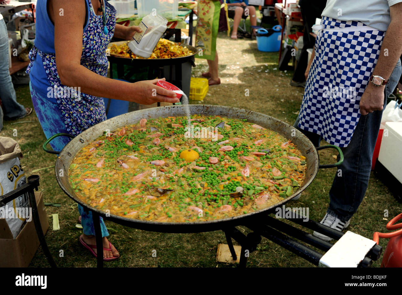 Woman cook adds salt to a large pan of paella being cooked at the Brunswick Festival in Hove Brighton UK Stock Photo