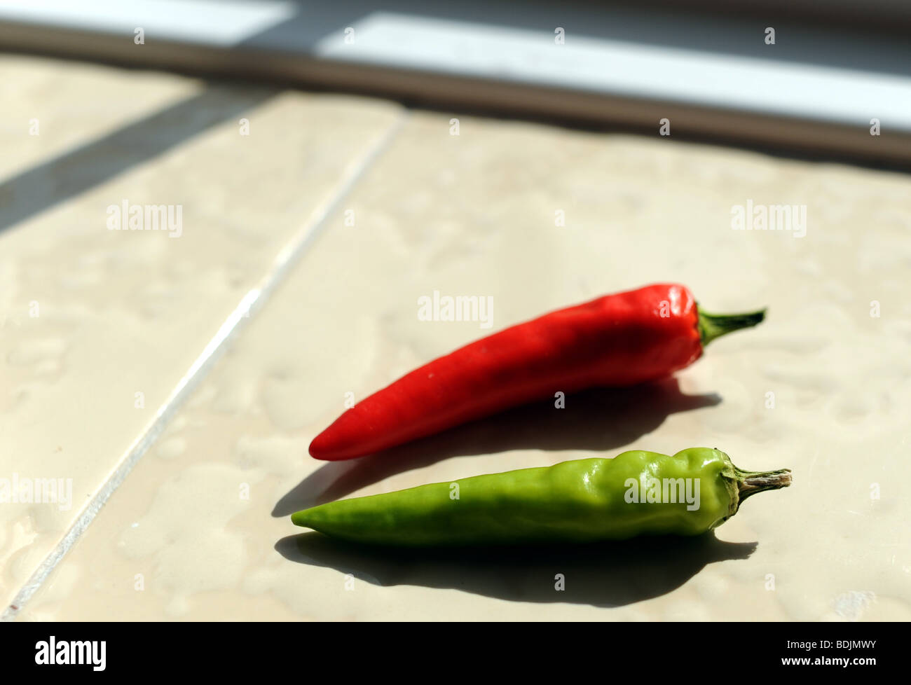 Green and red chilli peppers on a windowsill ripening in the sun Stock Photo