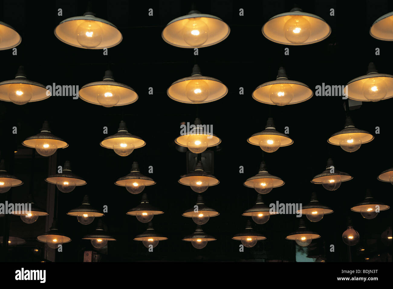 An array of identical electric lights that look like alien flying saucers against black celiing Stock Photo