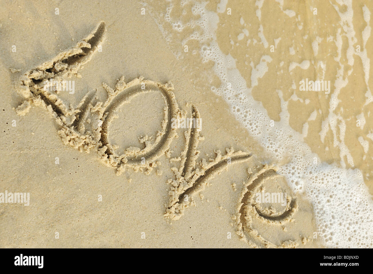 Inscription 'love' on sand. Sea coast with a rolling wave on an inscription Stock Photo