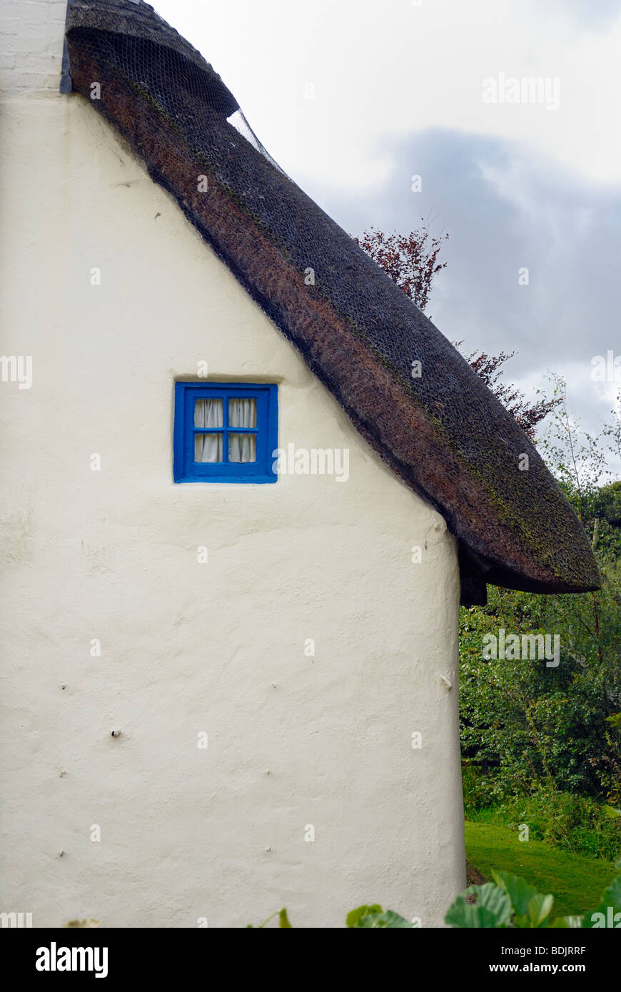The end of an old thatched cottage with a small blue window Stock Photo
