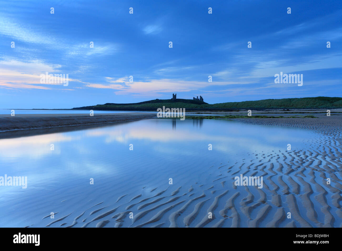 Dawn Embleton Bay, Dunstanburgh Castle on the horizon. Sunrise Northumberland coastal scene, reflections in pool. Stock Photo