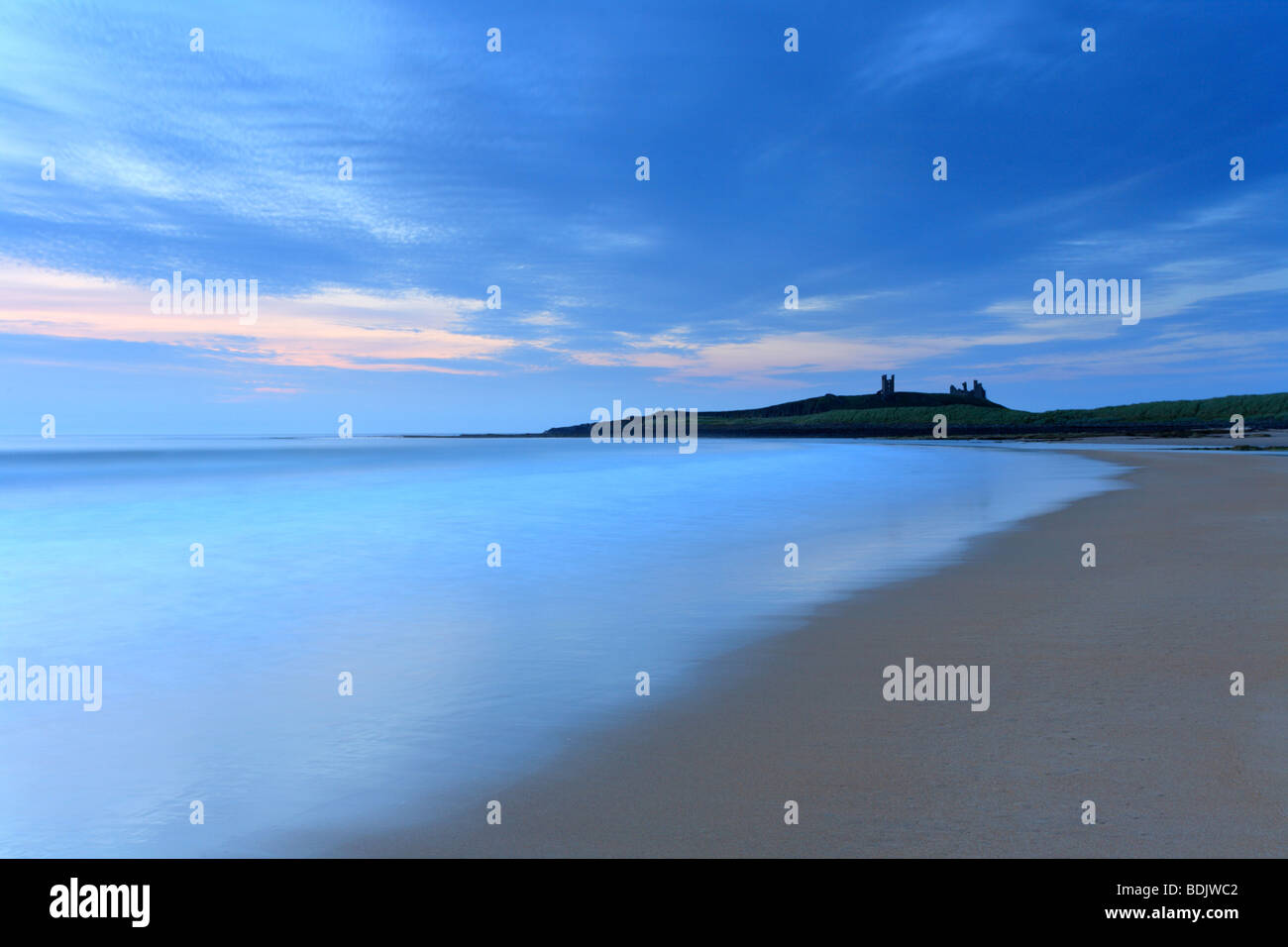 Dawn Embleton Bay, Dunstanburgh Castle on the horizon. Sunrise Northumberland coastal scene. Stock Photo