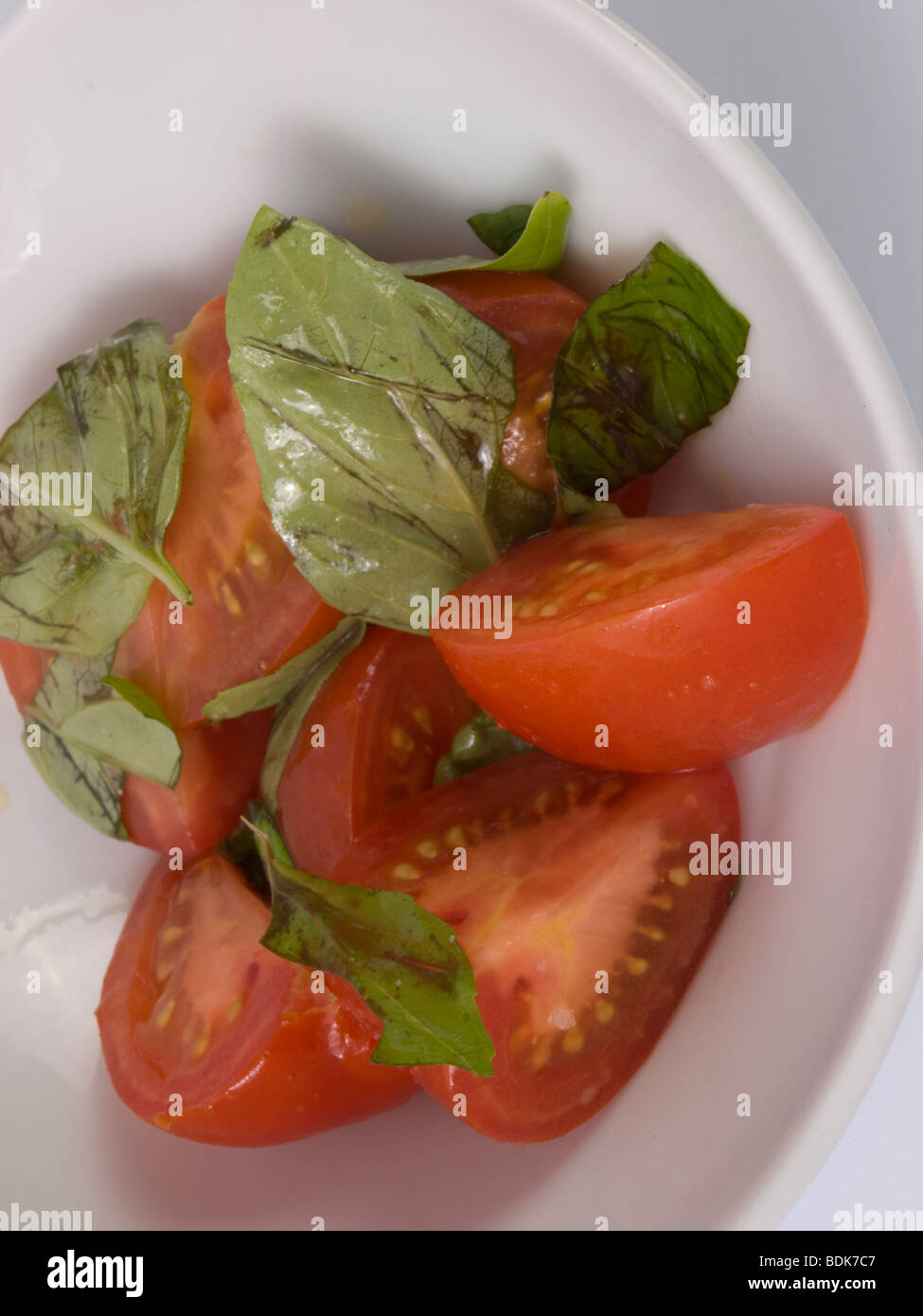 sliced tomatoes with oil and basil leaves in a bowl Stock Photo - Alamy