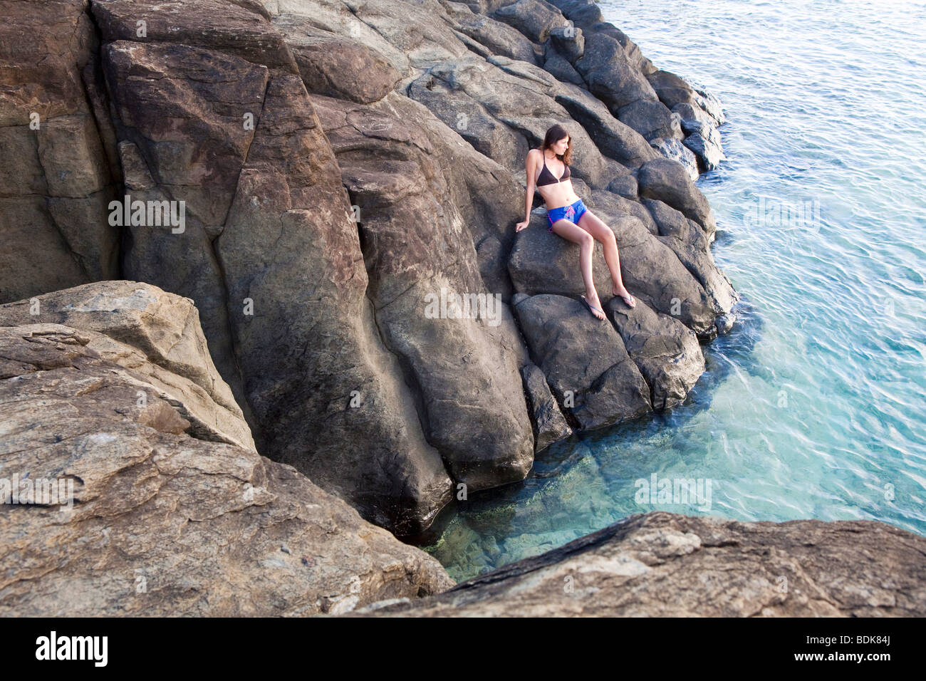 Model posing on a rock by the ocean on Rarotonga in The Cook Islands in The South Pacific Stock Photo