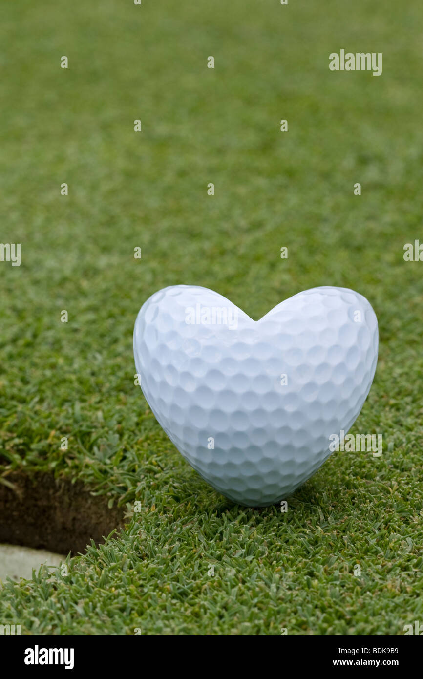 Heartshaped golf ball sitting next to the hole on a putting green