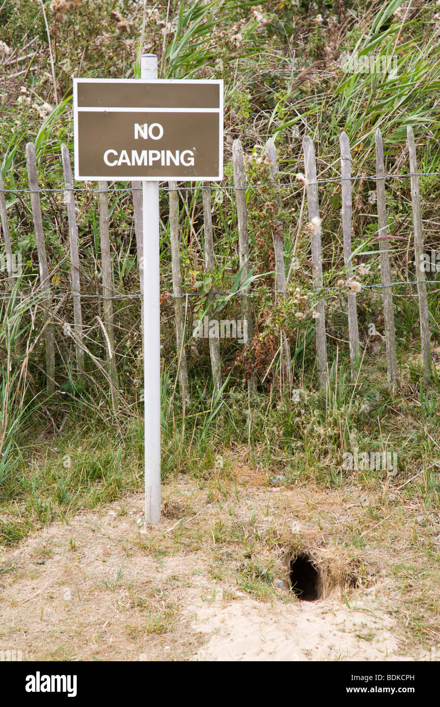 'No Camping' sign next to a 'rabbit hole'. Stock Photo