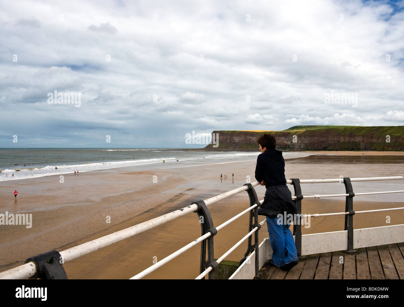 Woman Stood On Pier Watching Surfers Stock Photo