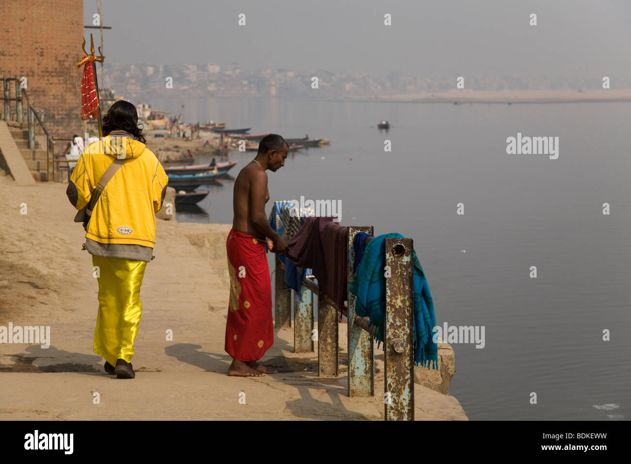 A Sadhu walks along the riverside in the city of Varanasi (Benares). The Sadhu holds a trident, the other man wears a dhoti. Stock Photo