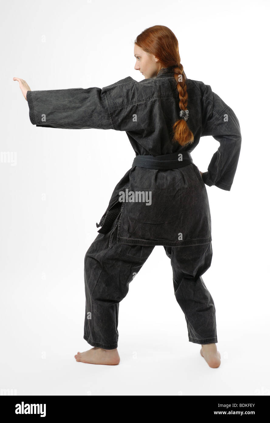 Girl in black uniform stands back on half-bent legs, left hand lifted for obstructing, isolated on white Stock Photo