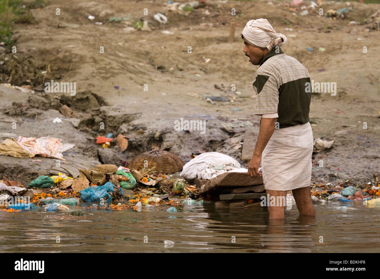 A dhobi (laundry man) washes clothes on the banks of the Ganga (Ganges) river in Varanasi, India. Stock Photo