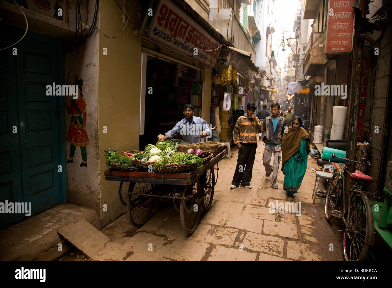 A handcart vendor pushes his cart loaded with vegetables along one of the narrow lanes (Gali) of Varanasi, India. Stock Photo