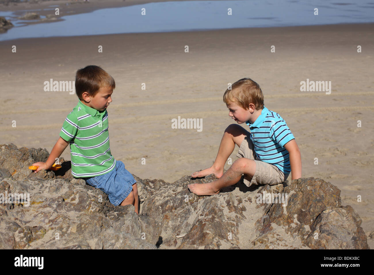 Two young boys sitting on rock at beach Stock Photo