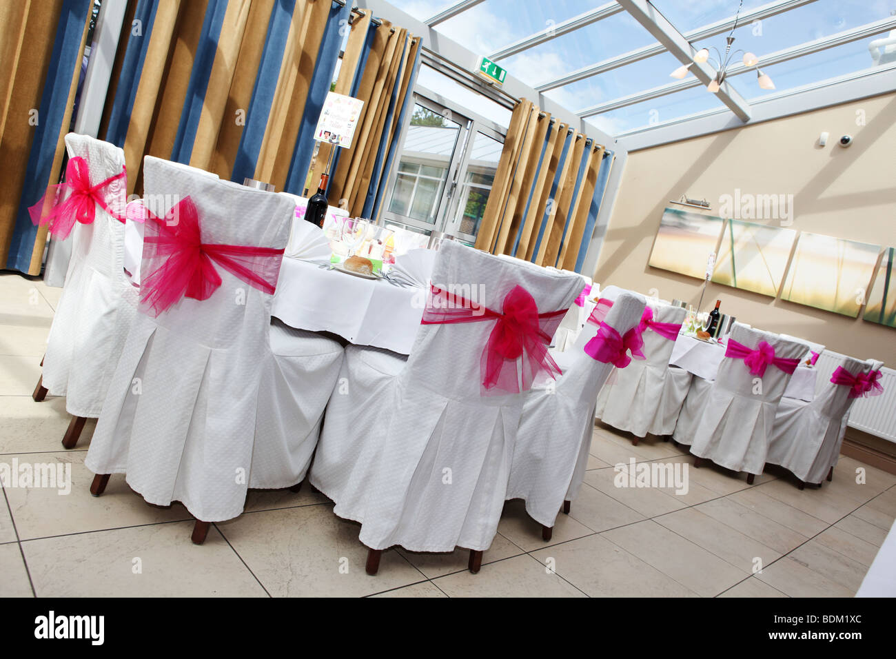 Wedding day chair covers with bright pink bows in hotel reception room conservatory prepared for wedding reception Stock Photo