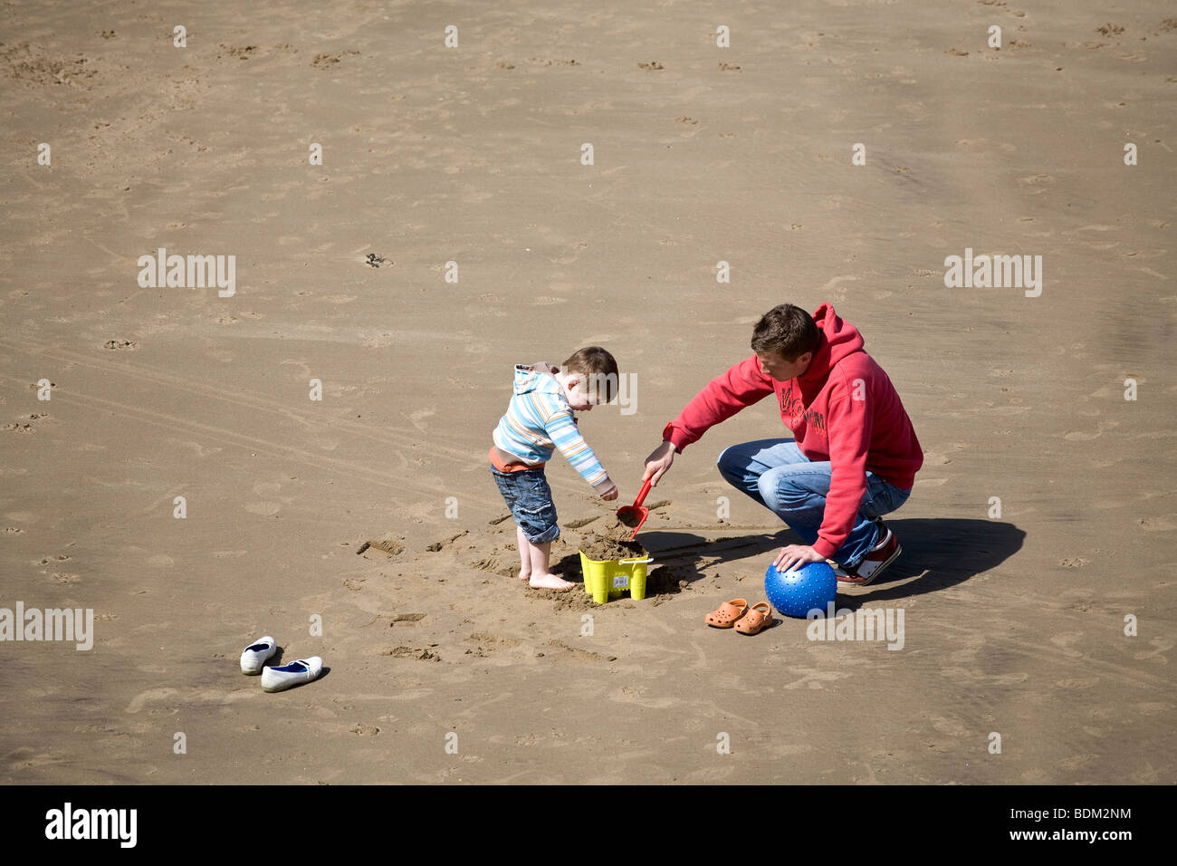 A young boy plays with his bucket and spade with his uncle on the beach