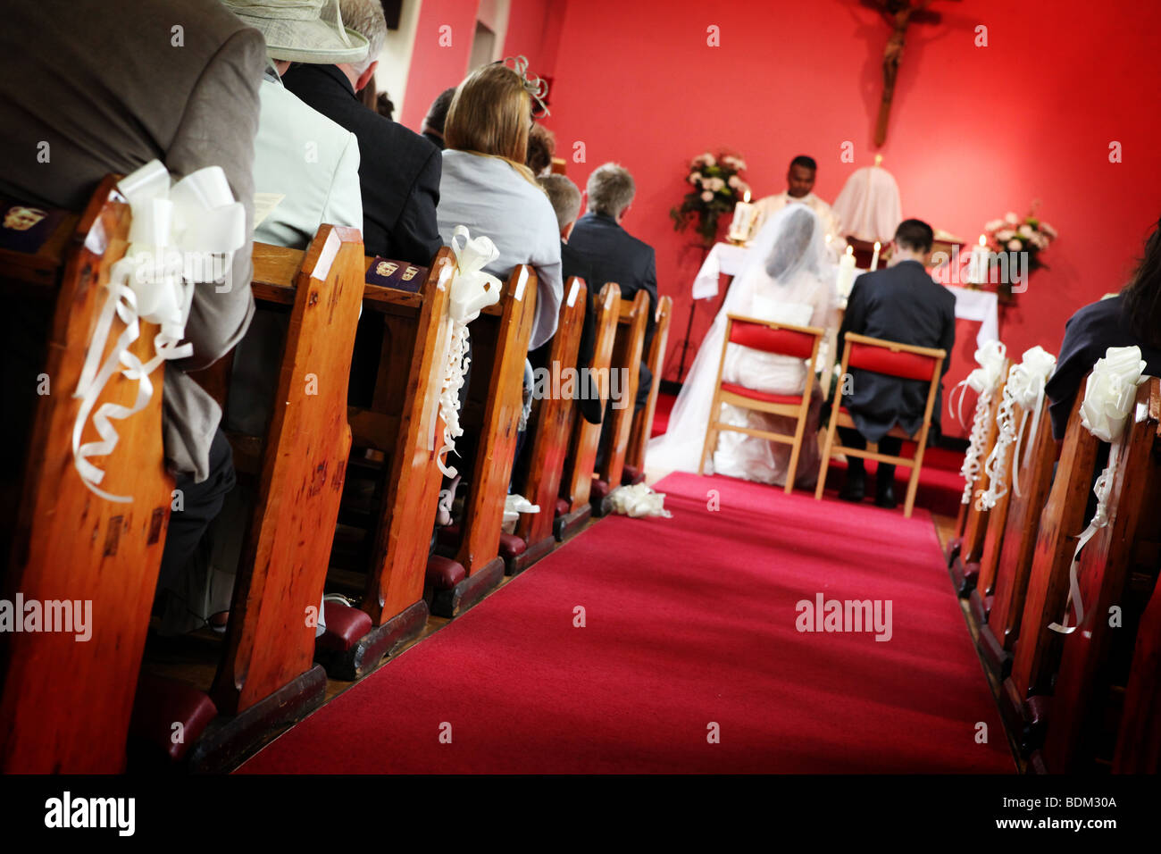 Church isle with red carpet and bride and groom sitting down in wedding ceremony at altar reportage style wedding photo image UK Stock Photo