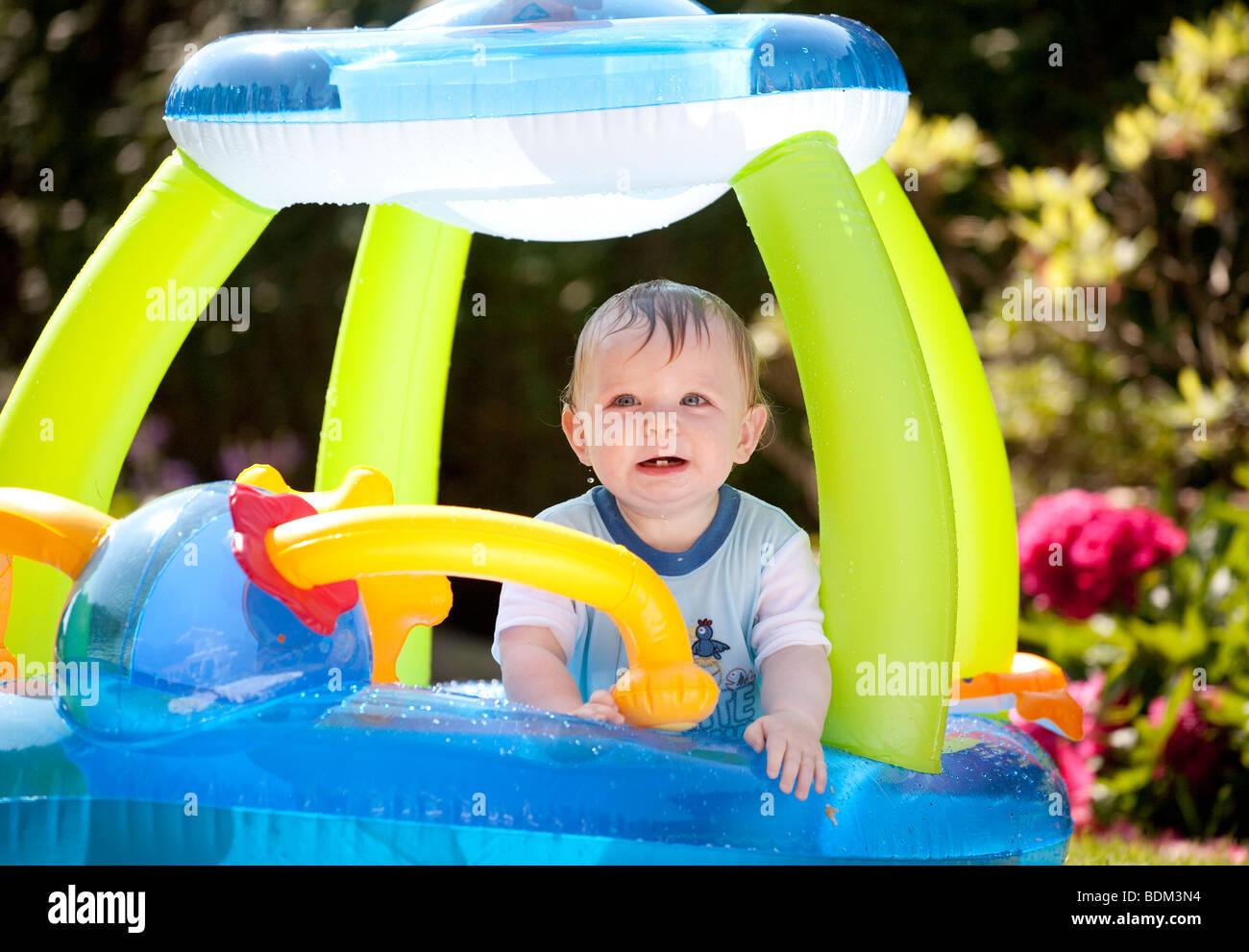 A baby boy playing in an inflated plastic boat paddling pool on a
