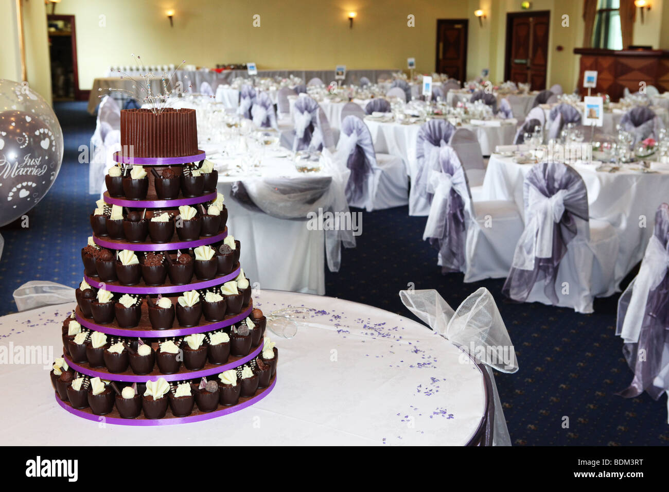 Modern wedding cake with individual chocolate cup cakes standing in wedding breakfast reception room on wedding day Stock Photo