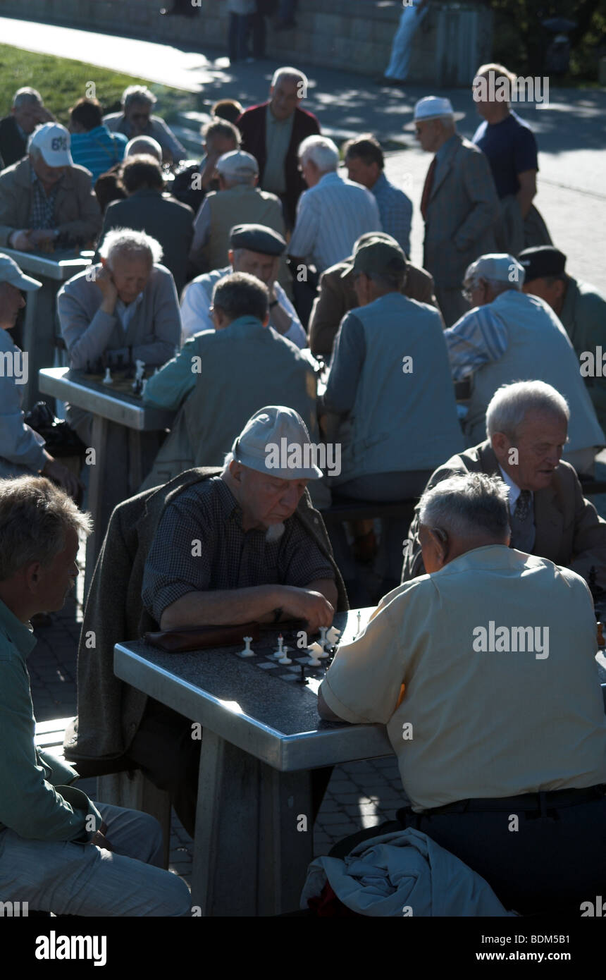 Elderly men gathered at several outdoor tables playing chess in public area Stock Photo