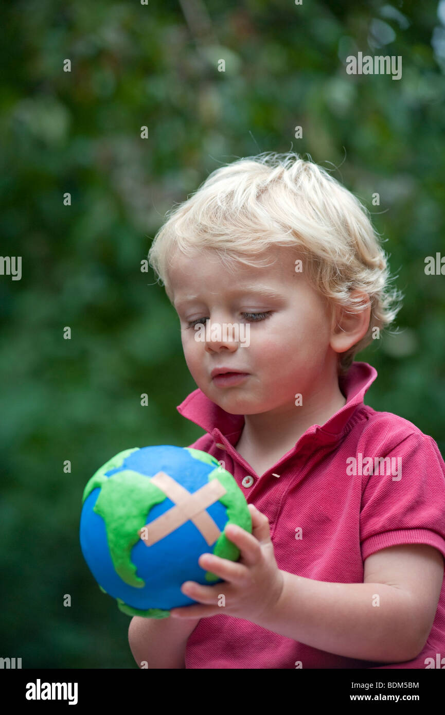 Young boy holding a model of a sick planet Earth with a Band Aid attached Stock Photo