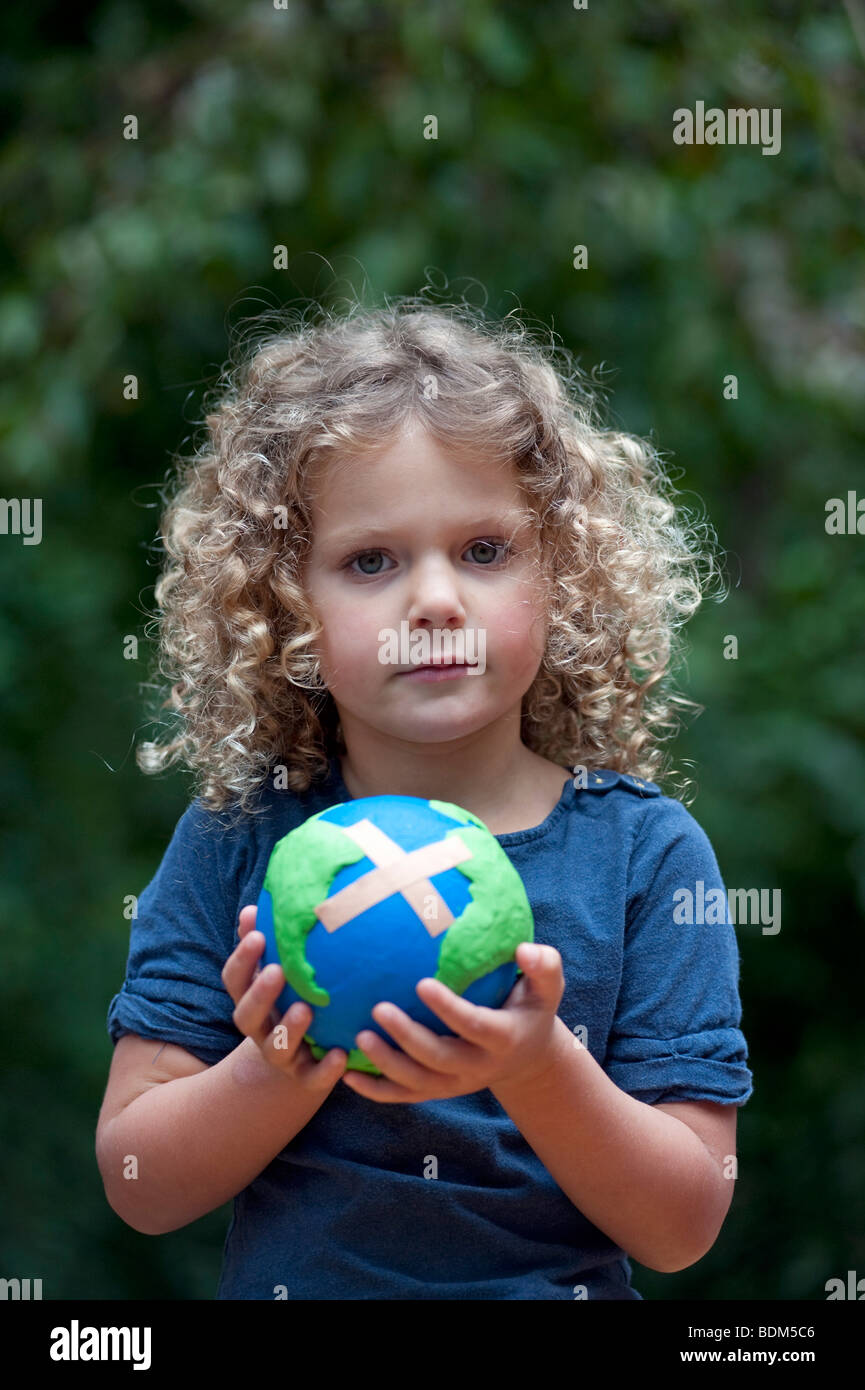 Young girl holding a model of a sick planet Earth with a Band Aid attached Stock Photo