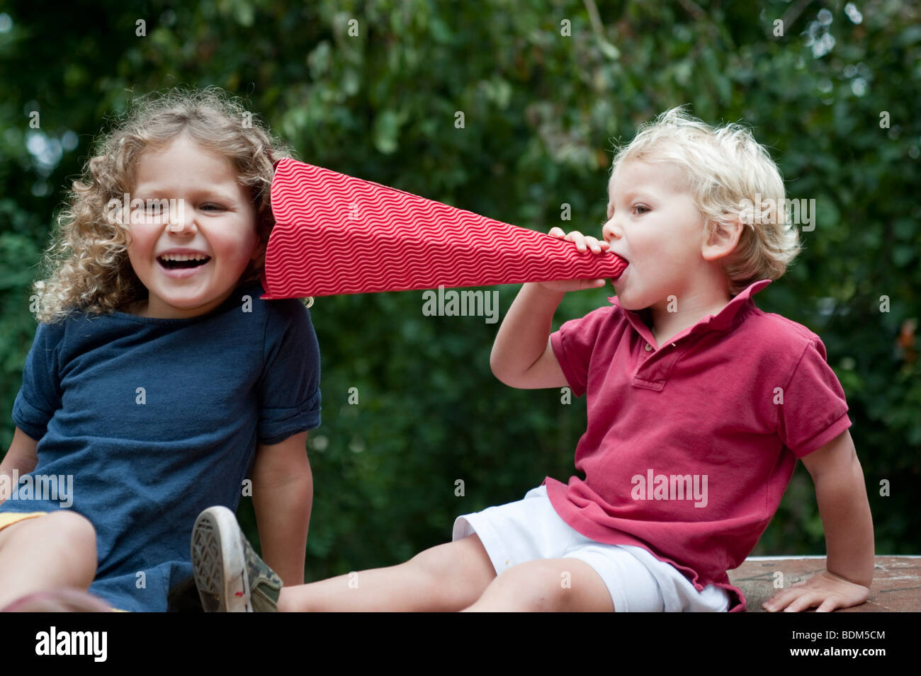 Two young children talking and laughing using homemade megaphone Stock Photo