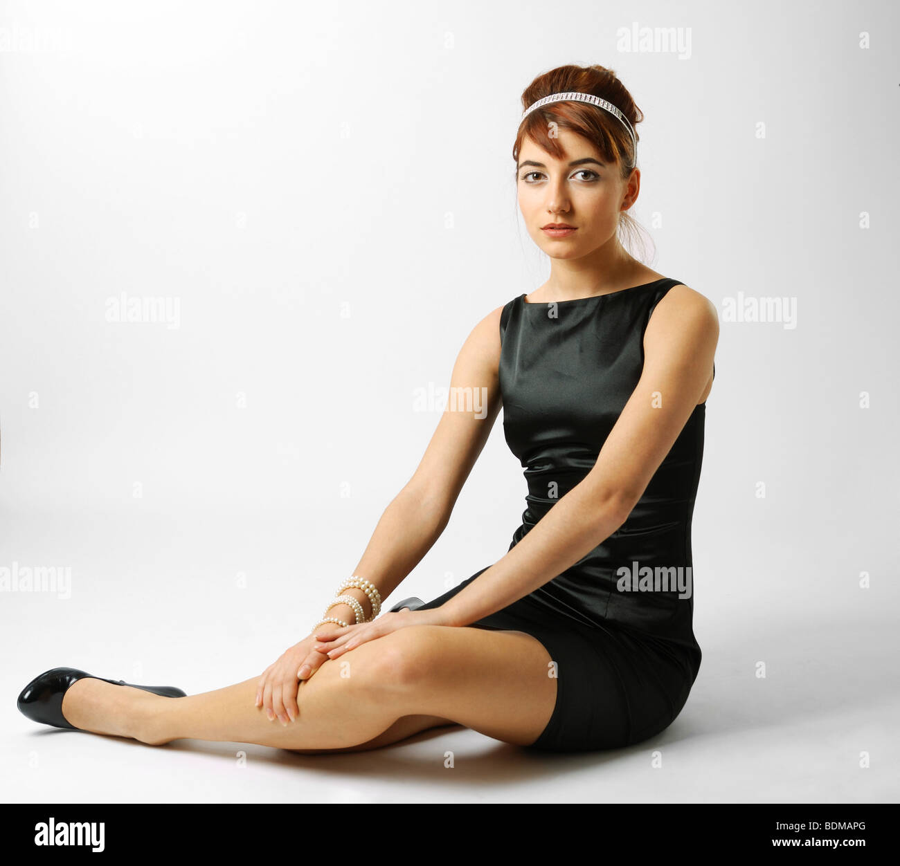 Smart girl sits on the floor sideways in little black dress Stock Photo