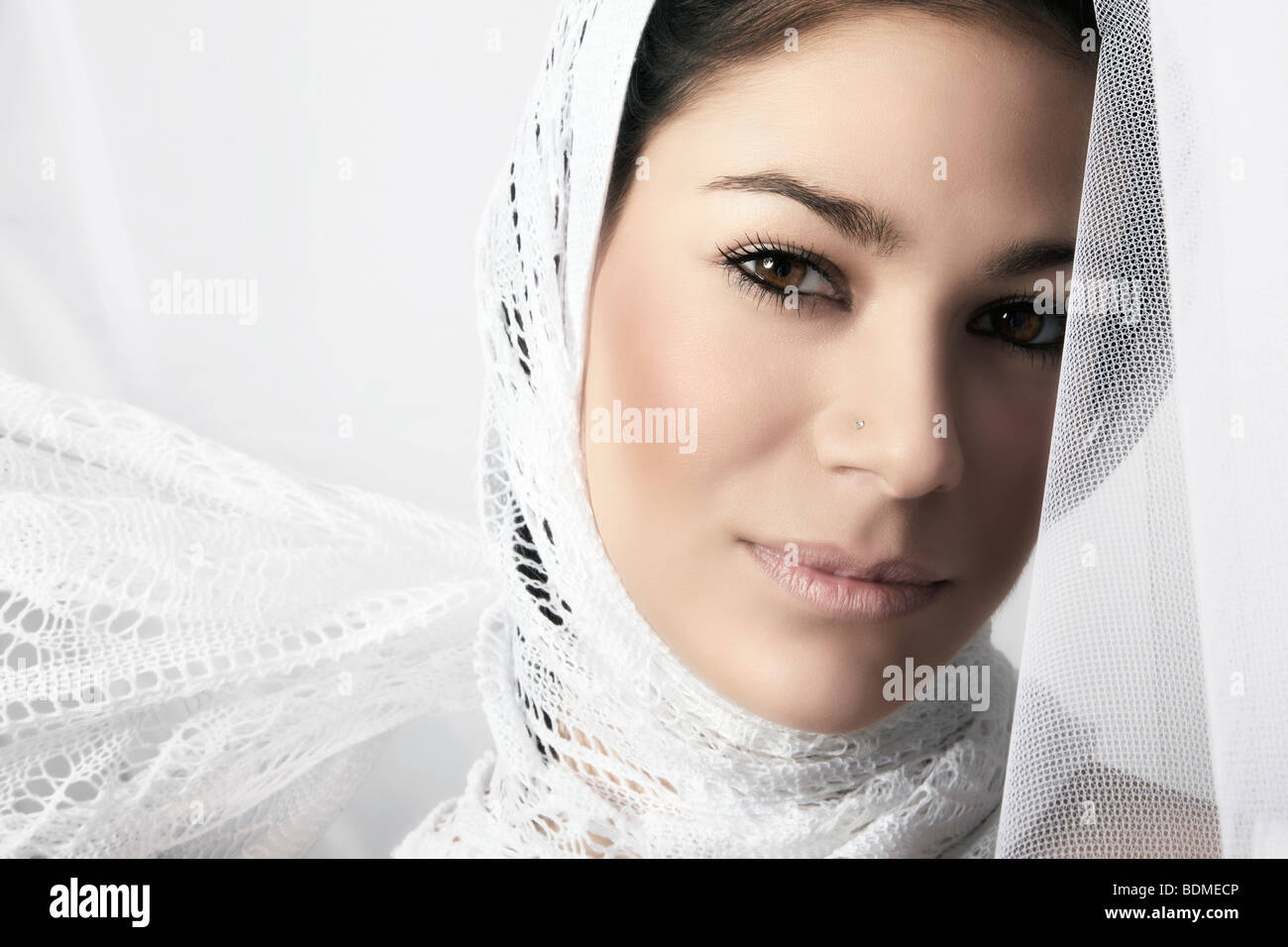 Portrait of a young dark-haired woman with head scarf, wrapped in a white cloth and looking at the viewer Stock Photo