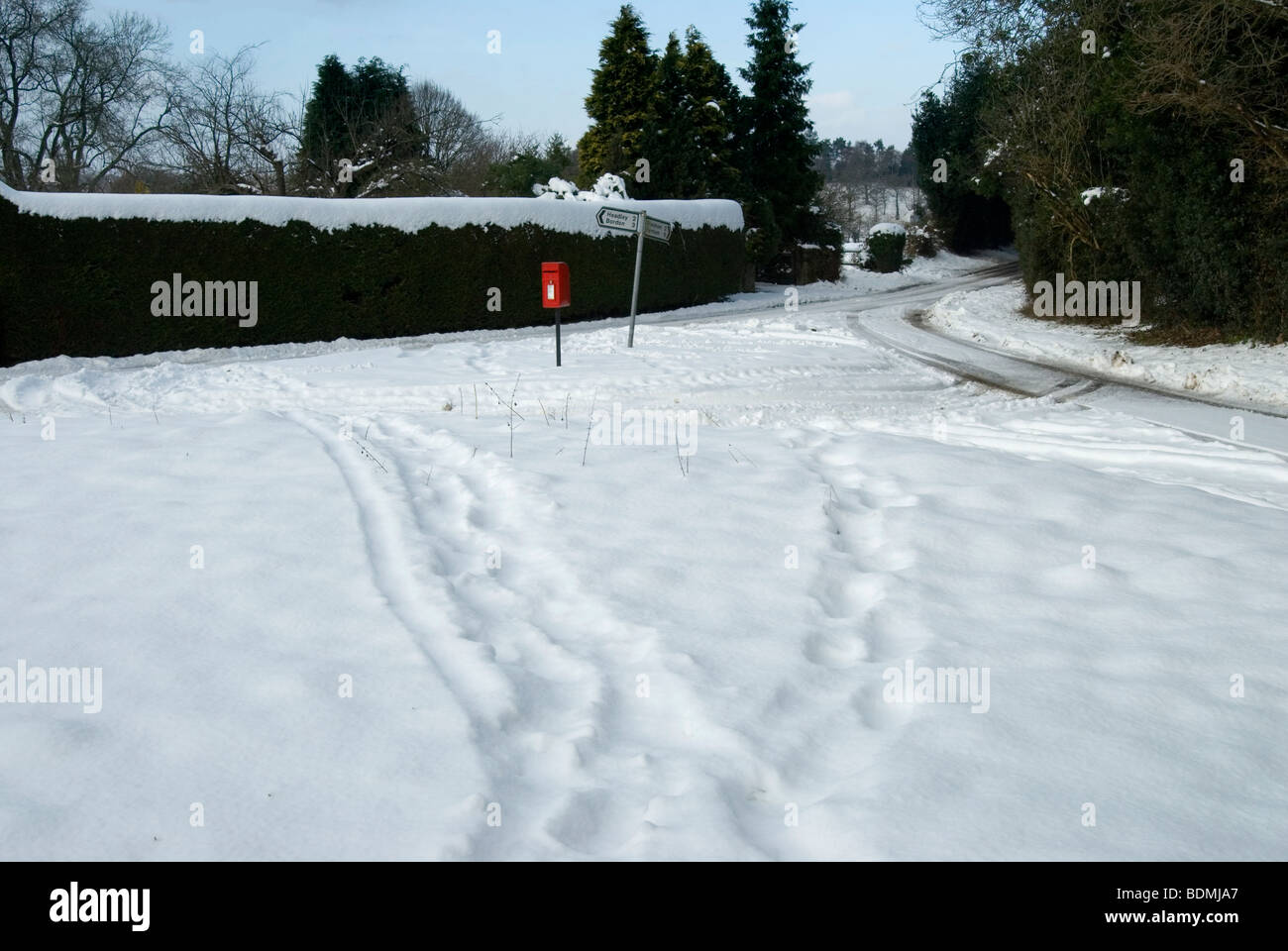 Christmas card snowy landscape scene with footprints and a red letter box and road sign Stock Photo