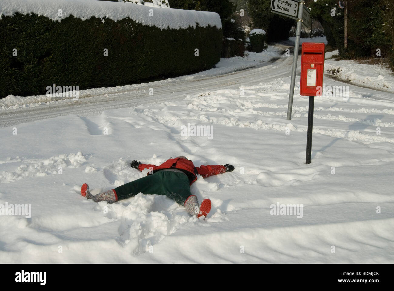 Person lying in the snow forming the letter X next to a red post office letter box Stock Photo