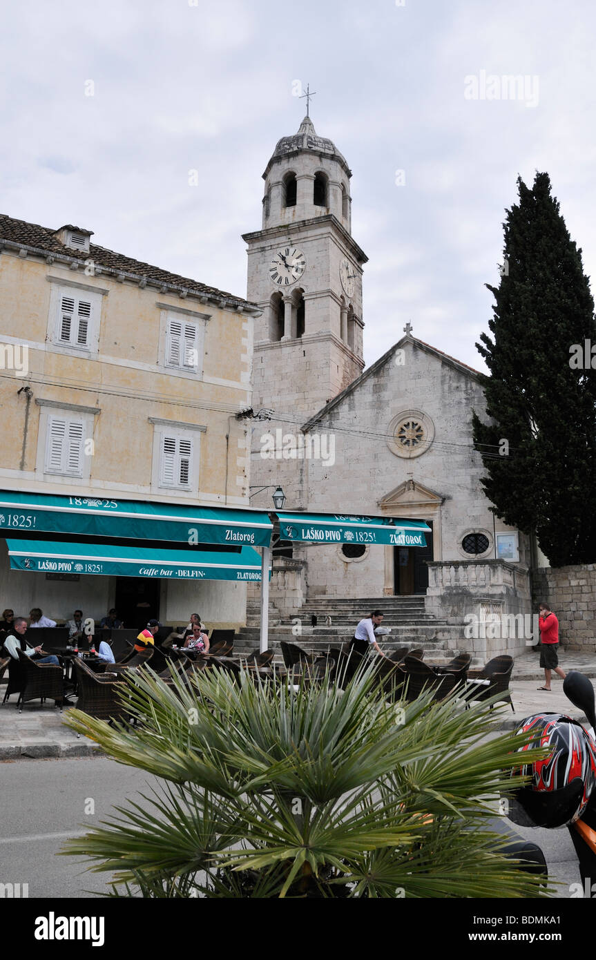 A grey church and its imposing clock tower overlook a comfortable pavement restaurant in Cavtat Stock Photo