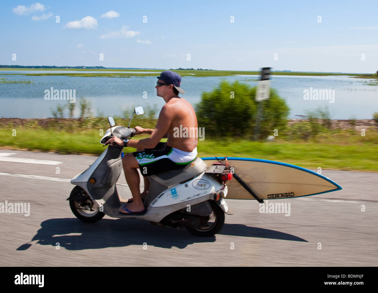 A surfer with his surfboard attached to a scooter rides along the ocean in Folly Beach, South Carolina. Stock Photo