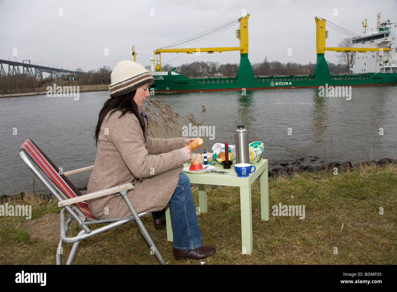 Young woman, 30-35 years, having breakfast on a damp winter day at the Kiel Canal, watching passing ships, Schleswig-Holstein,  Stock Photo