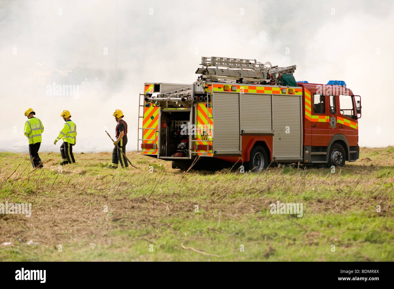 emergency services fire brigade attending a field fire full of thick smoke Stock Photo