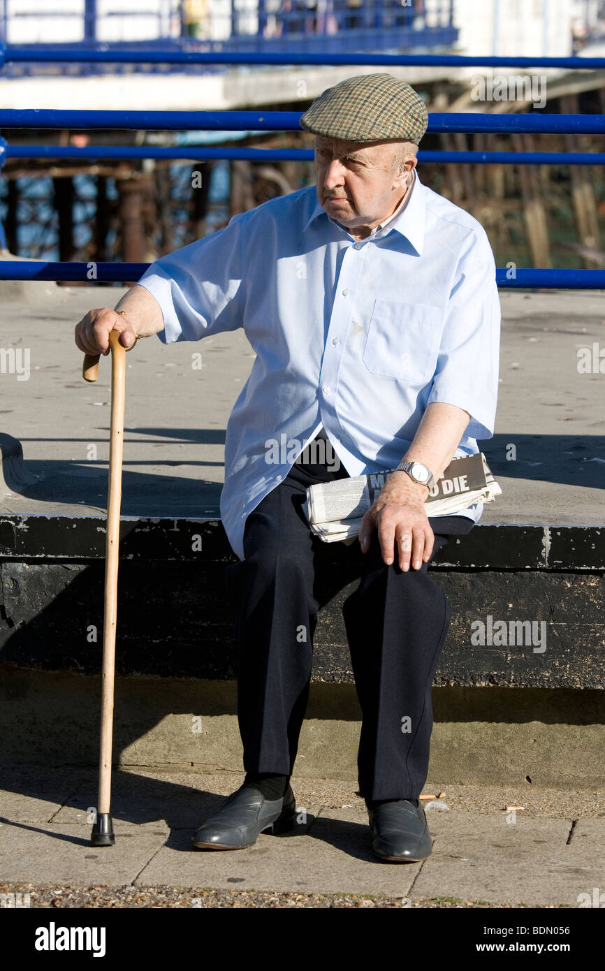 An elderly man sits with his walking stick. Stock Photo