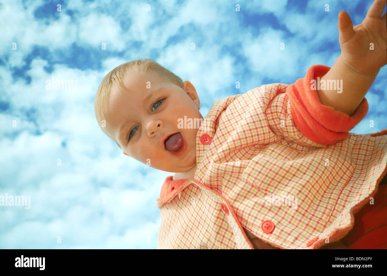 Toddler laughing after being thrown up into the air, against cloudy blue sky Stock Photo