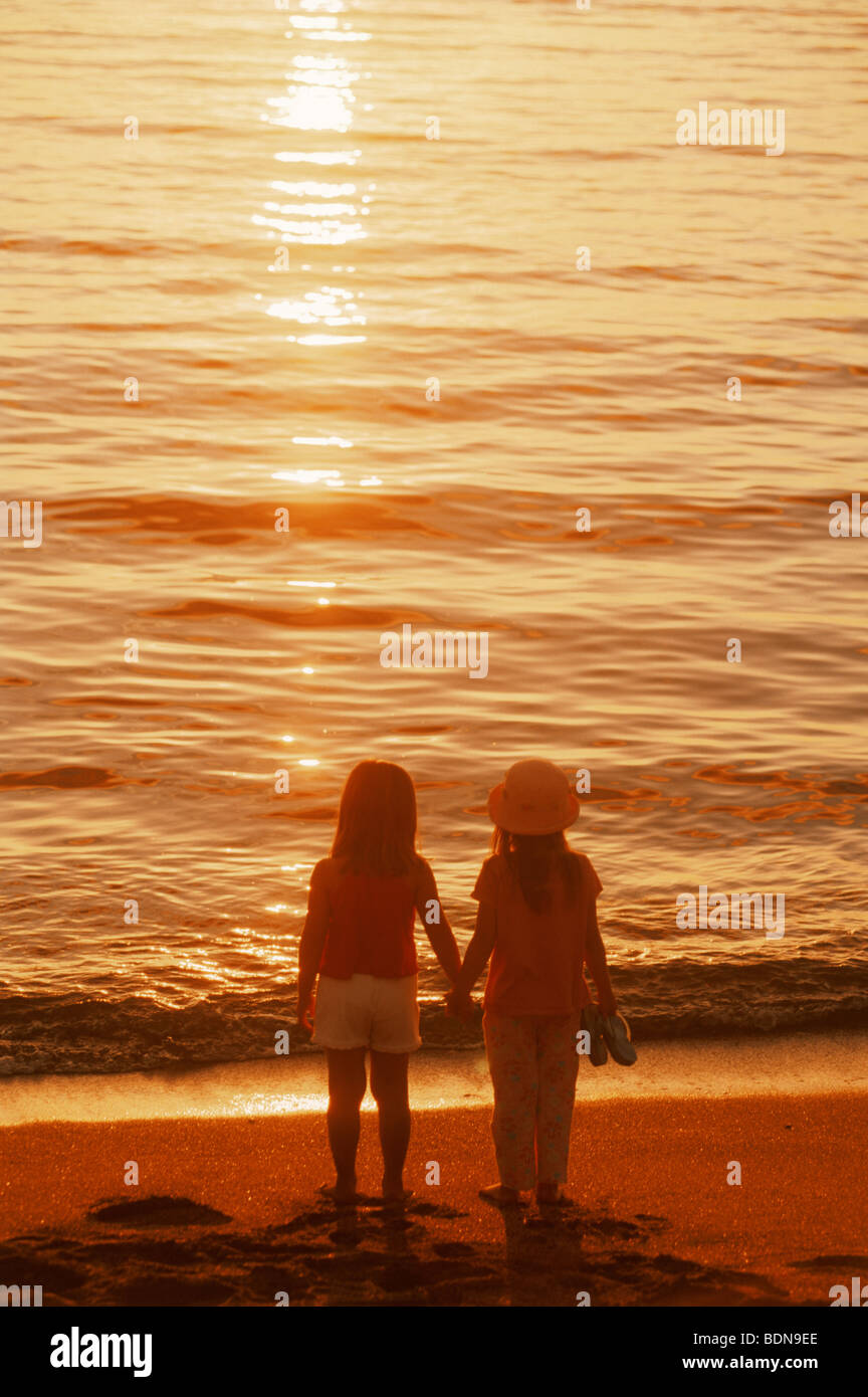 Two girls holding hands on sandy shore in sunset light Stock Photo