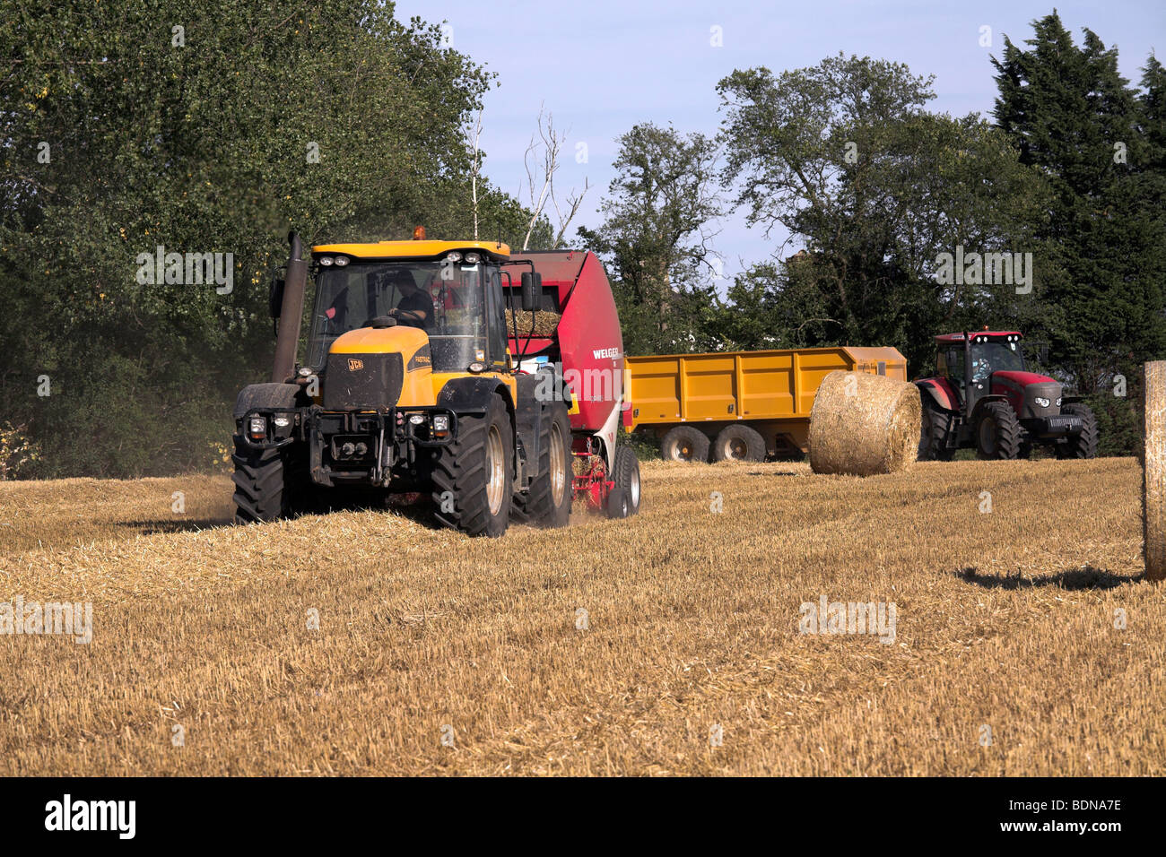Tractor and straw baler working in a field Stock Photo