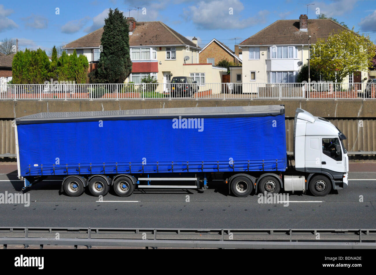 Articulated trailer and lorry in cutting on A12 dual carriageway passing semi detached houses Stock Photo