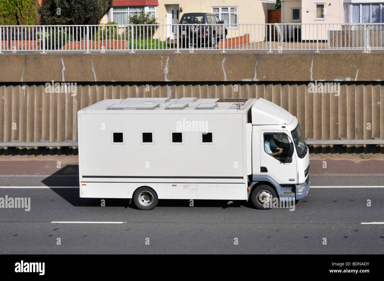 GSL prisoner delivery van on A12 dual carriageway passing semi detached houses with company name & logo digitally removed Stock Photo