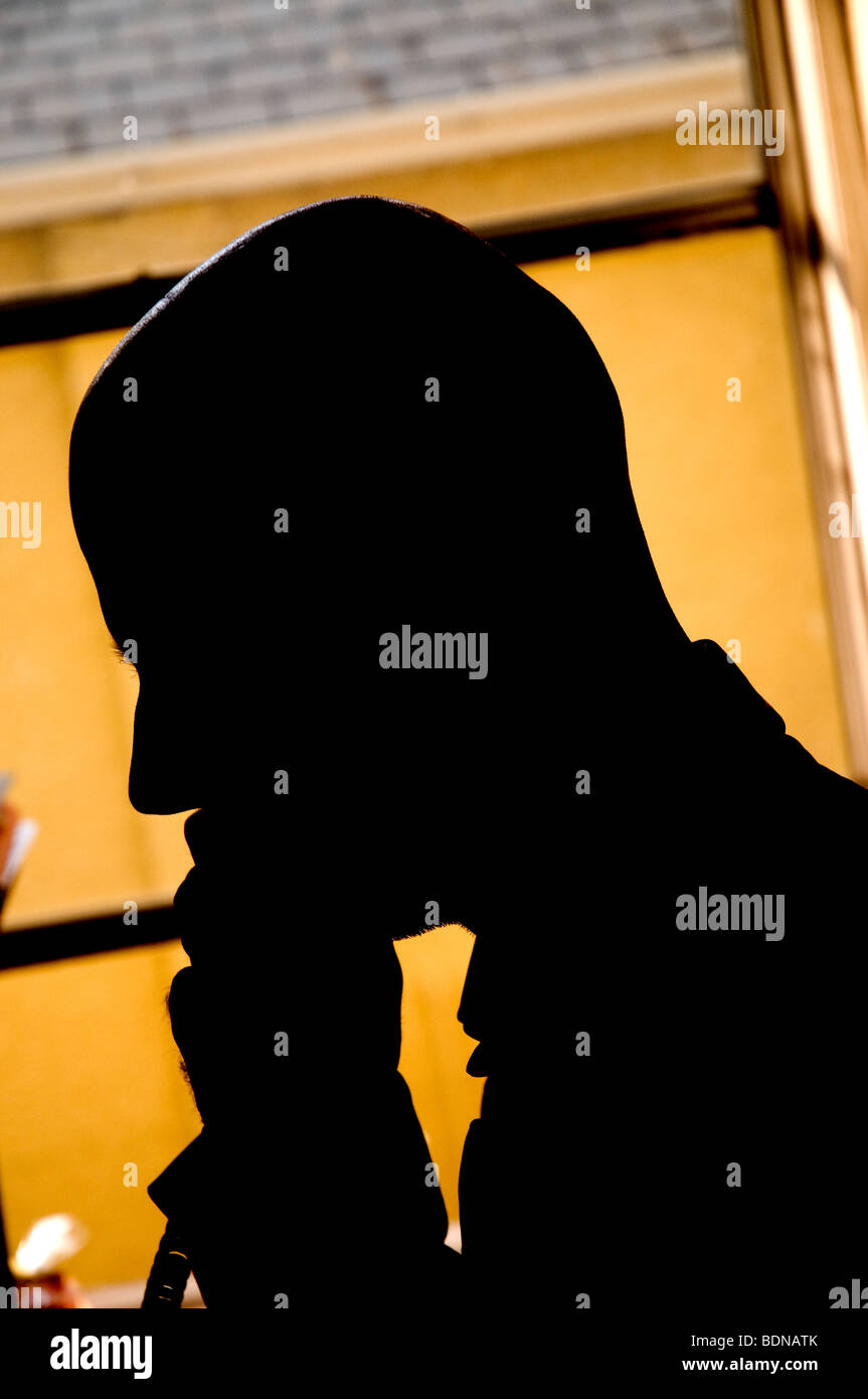 Silhouette of a man with a bald head answering  a telephone call in an office. Stock Photo
