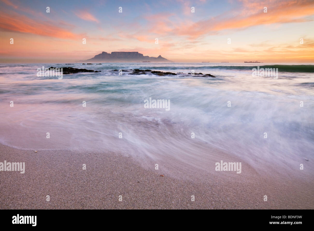 Surf on beach at Table Bay, with Table Mountain in background at sunset, Bloubergstrand, Western Cape Province, South Africa Stock Photo