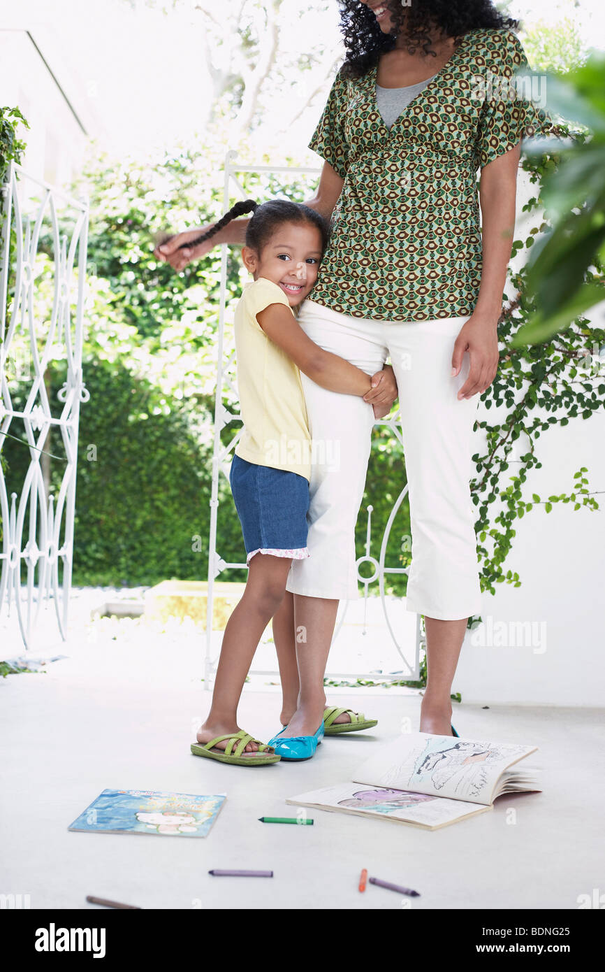 Girl (5-6 years) hugging mothers leg, standing on verandah Stock Photo