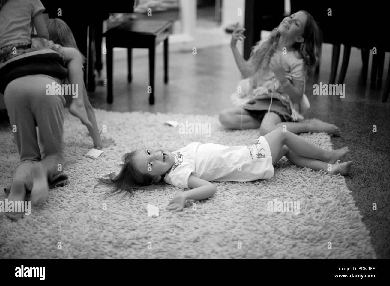 Black and white image of girls playing on rug in living room Stock Photo