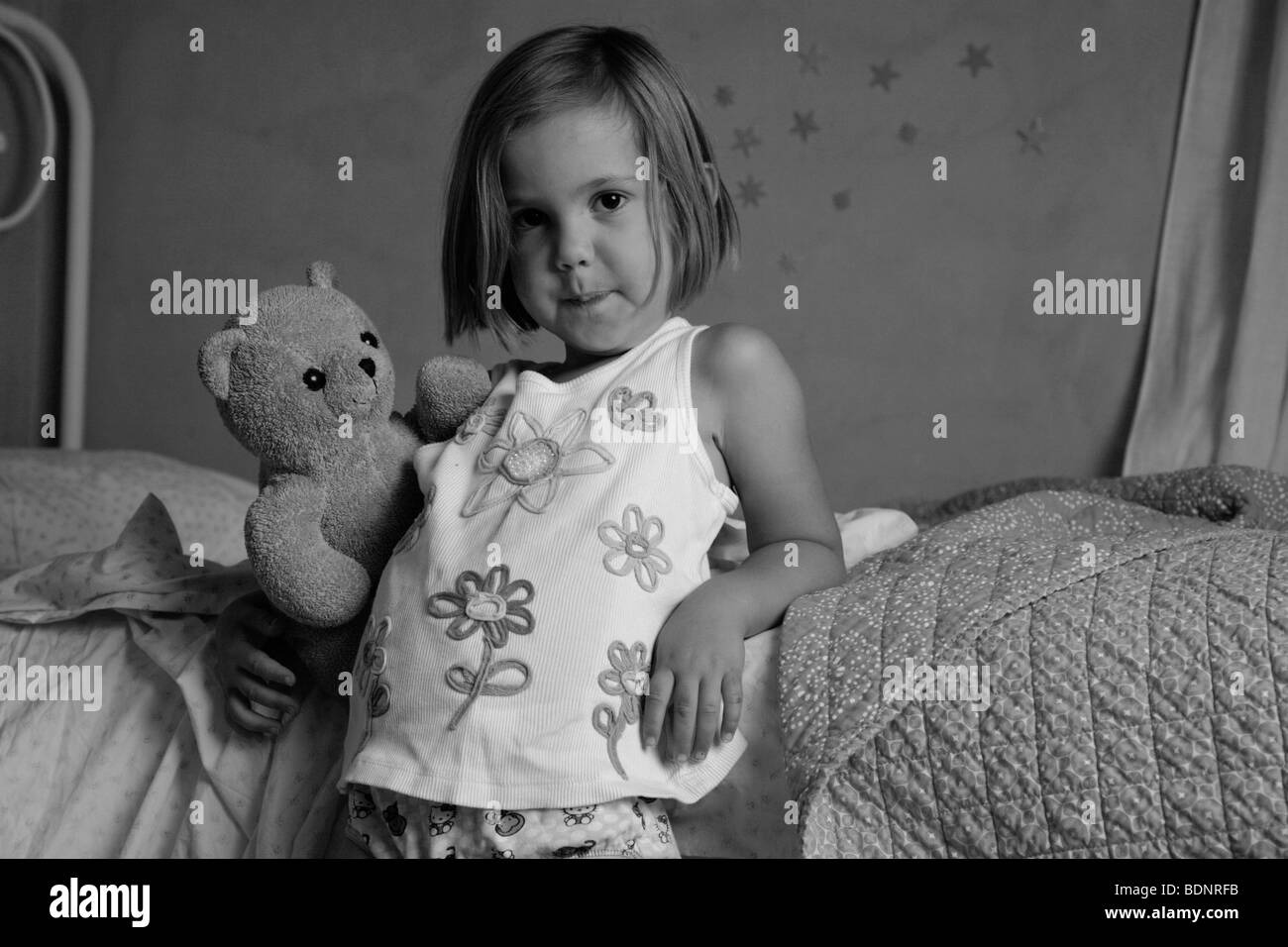 Black and white portrait of young girl holding teddy bear in bedroom Stock Photo