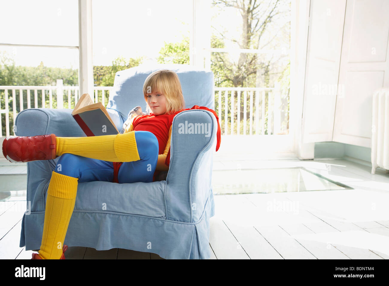 Young boy (79) sitting in armchair reading, wearing superhero costume
