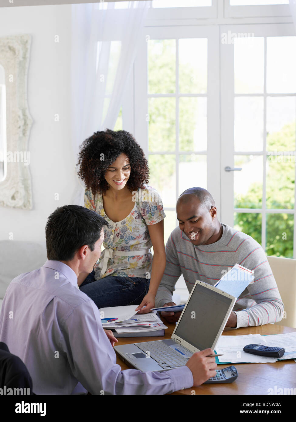 Young African American couple discussing home finances with financial advisor at dining room table Stock Photo