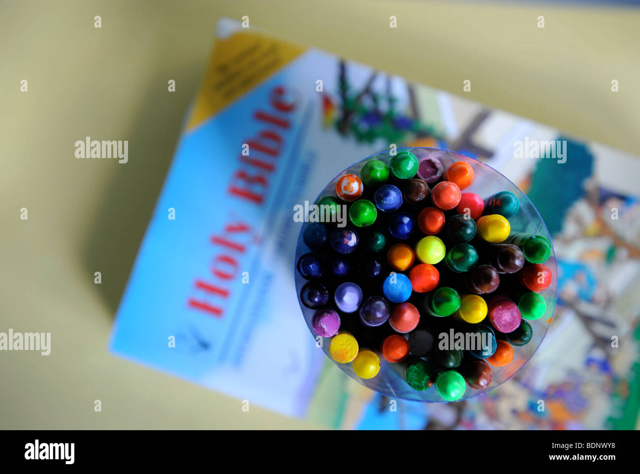 A COLLECTION OF COLOURED CHILDRENS CRAYONS WITH HOLY BIBLE AT A SUNDAY